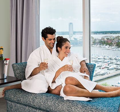 Couple drinking champagne in white bath robes overlooking the harbour